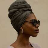 Woman wearing a green headscarf and sunglasses against a beige background
