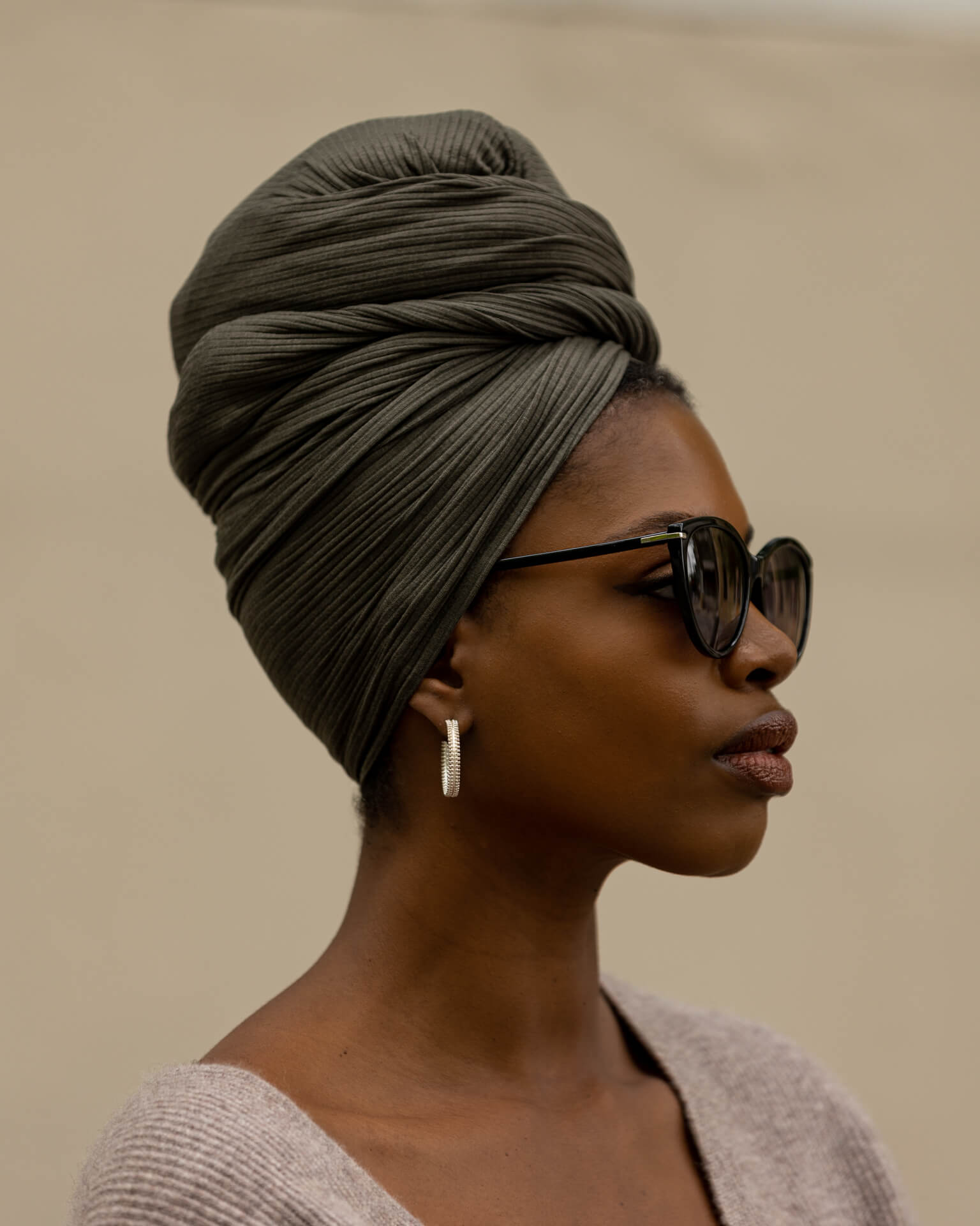 Woman wearing a green headscarf and sunglasses against a beige background
