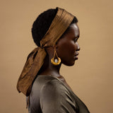 Woman wearing a brown headscarf and gold earrings against a beige background