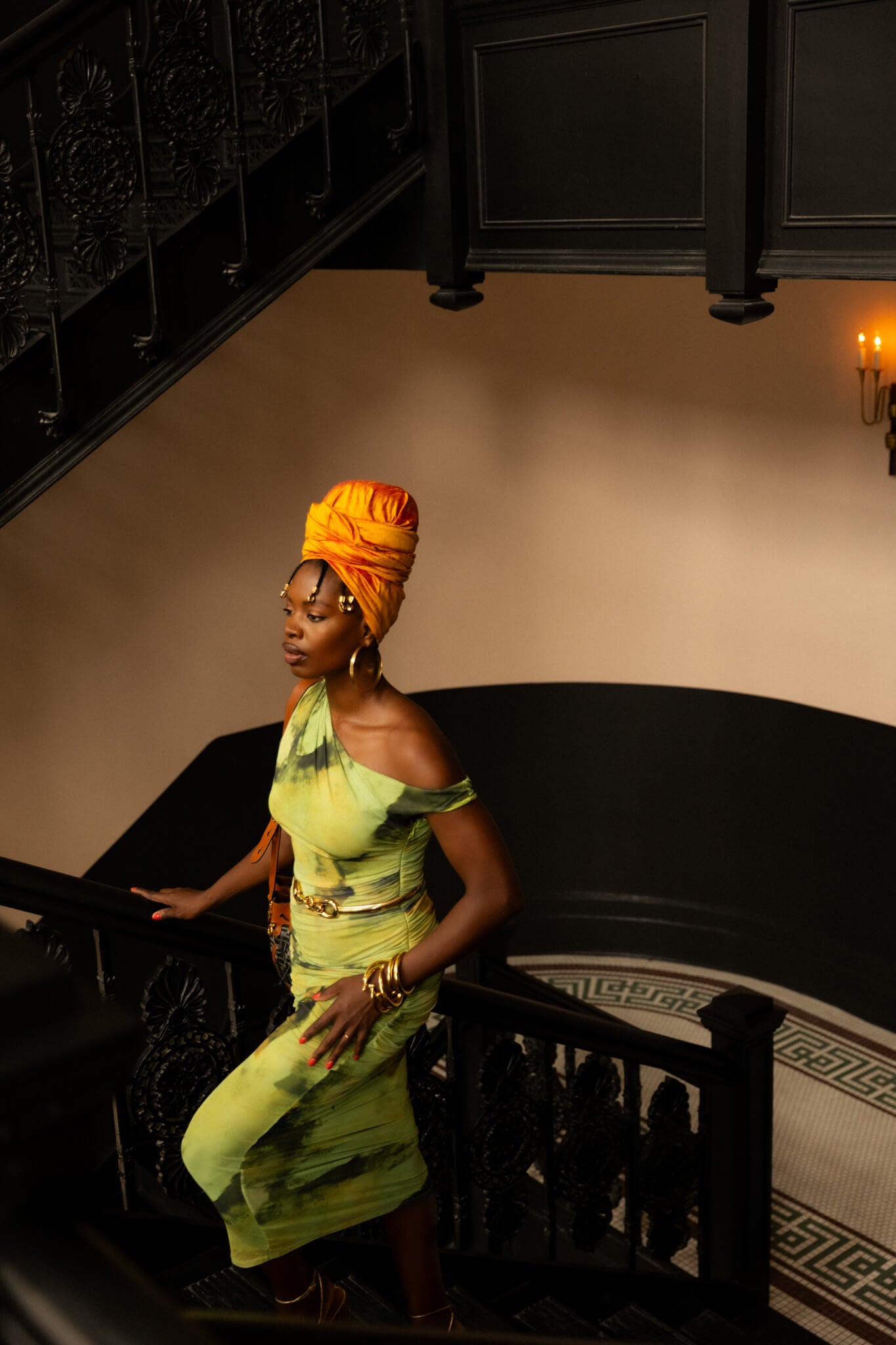 Woman in a green dress and orange headscarf standing on a staircase.