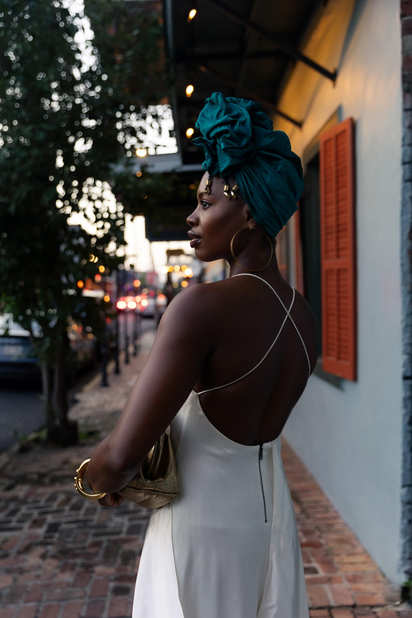 Woman in a white dress with a teal headscarf standing on a street.