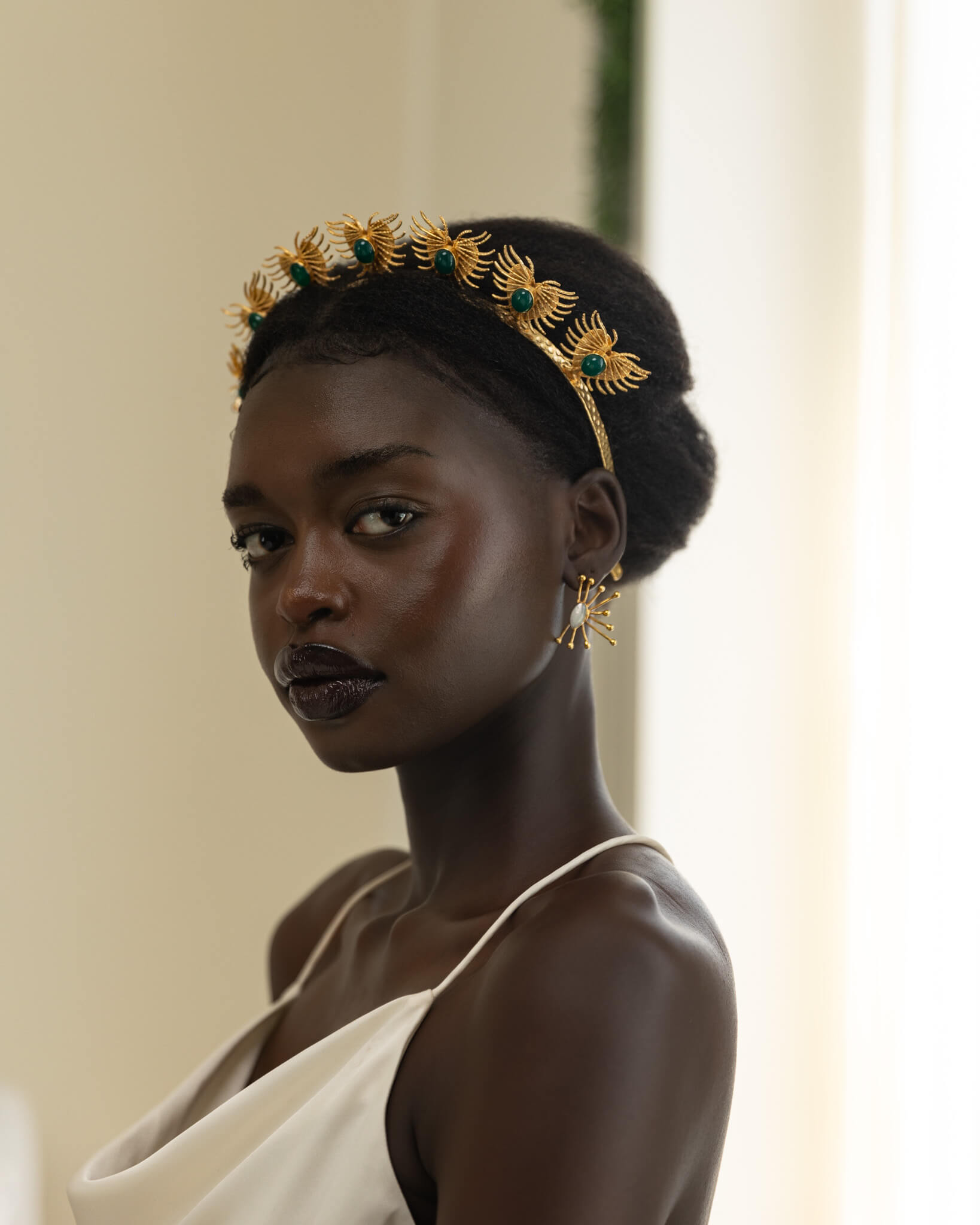 Woman wearing a gold headpiece with green stones against a neutral background