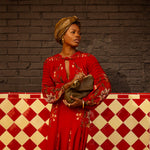 Woman in a red dress with gold accents standing against a brick wall with a checkered floor.