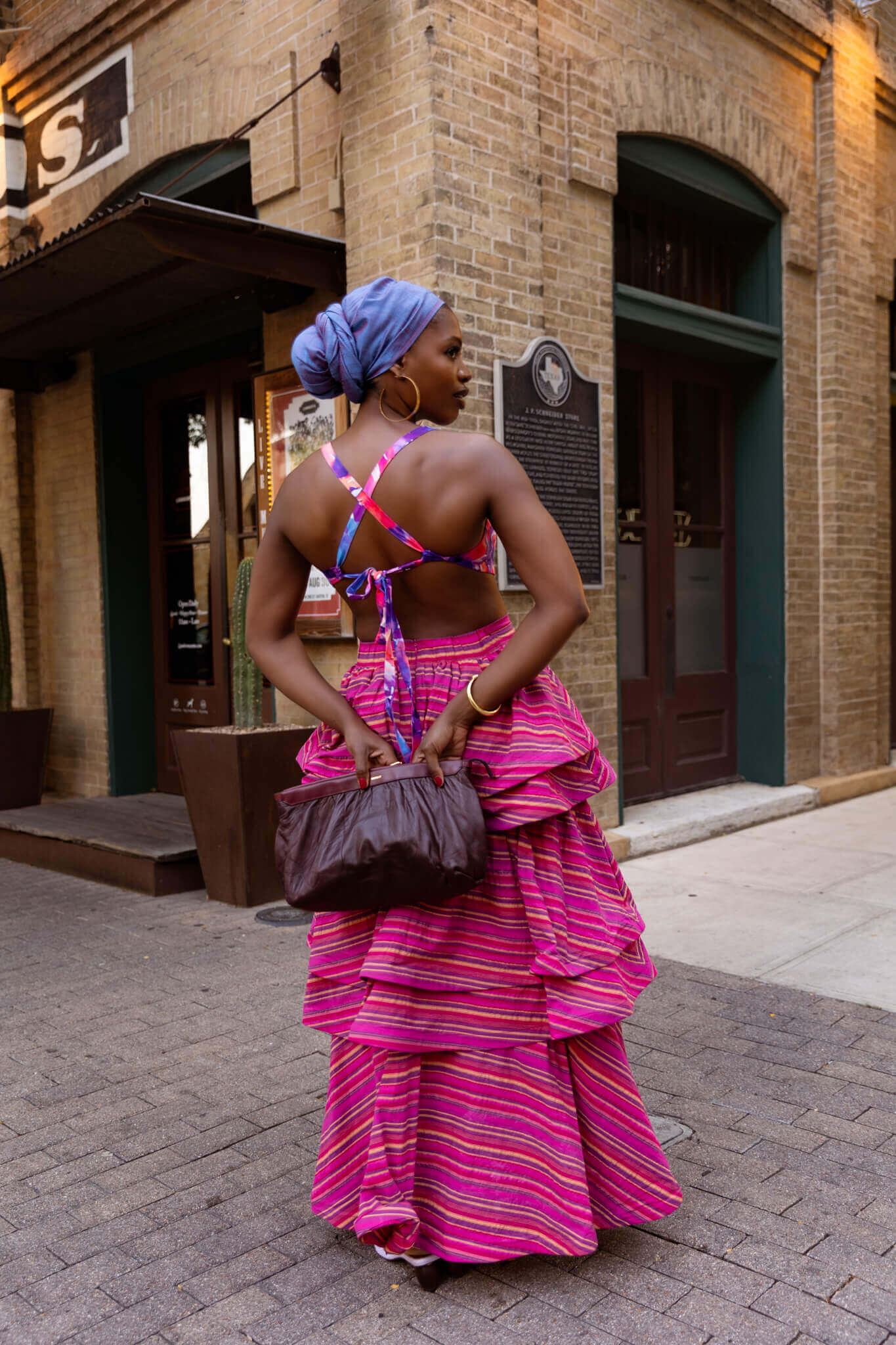 Woman in a colorful dress standing on a sidewalk in front of a brick building.