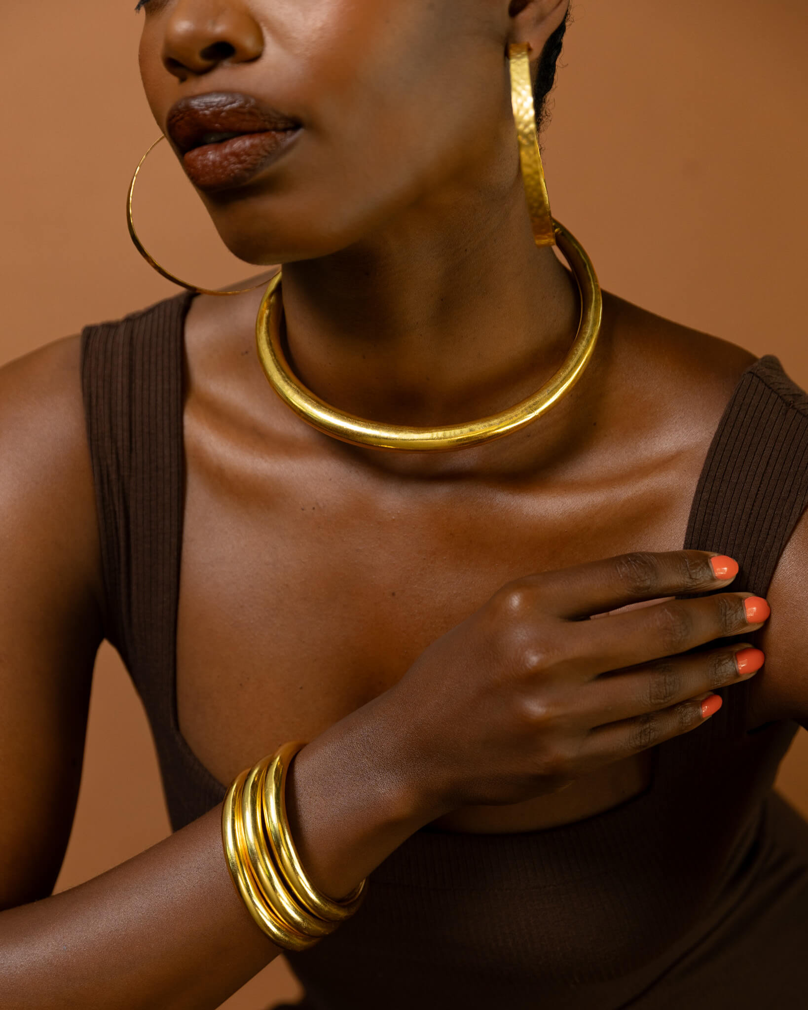 Woman wearing gold jewelry against a brown background