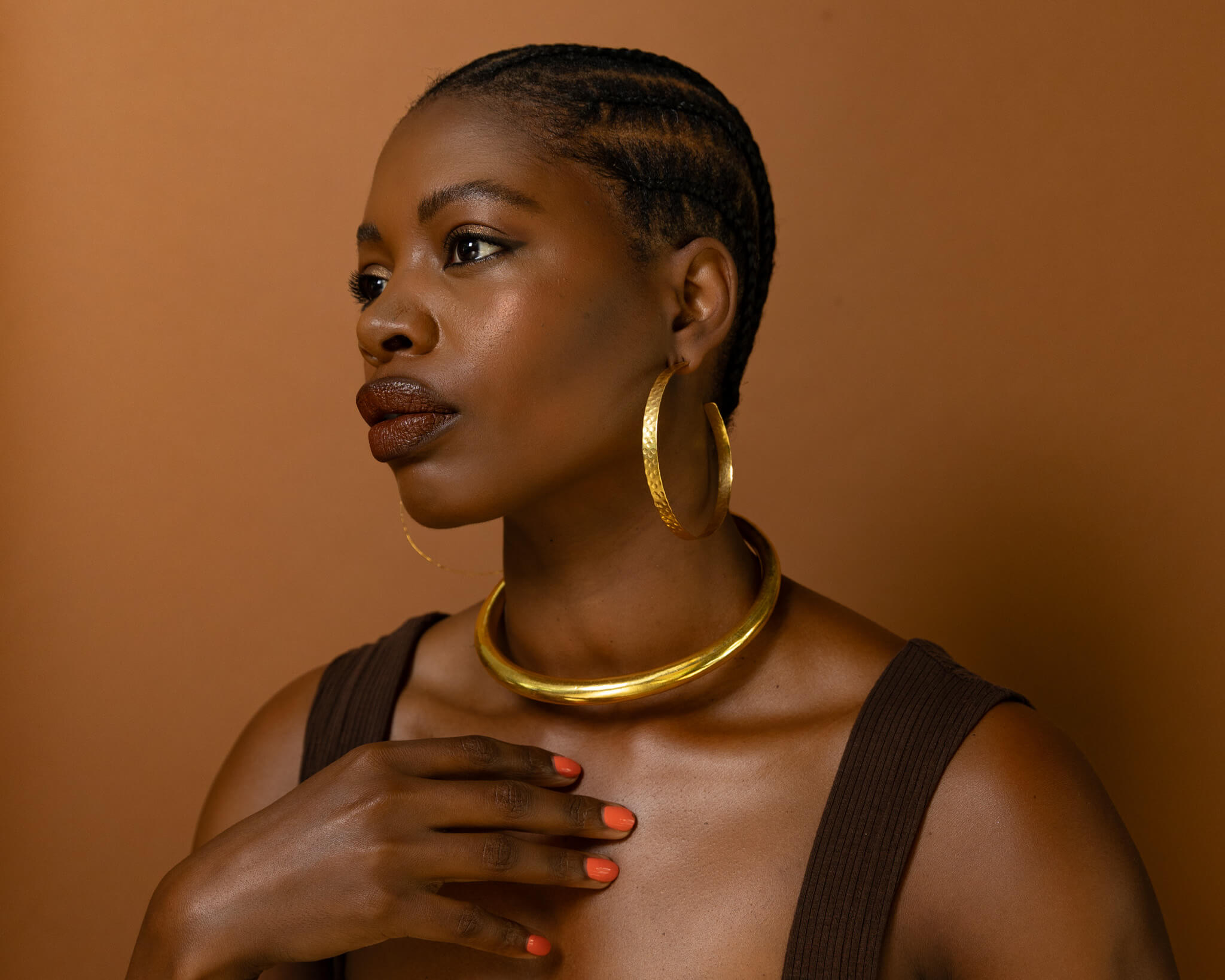 Woman wearing gold jewelry against a brown background